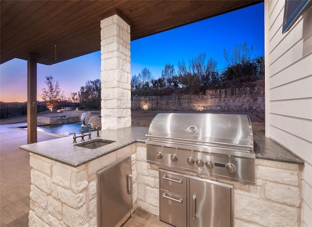 patio terrace at dusk with an outdoor kitchen, area for grilling, and sink