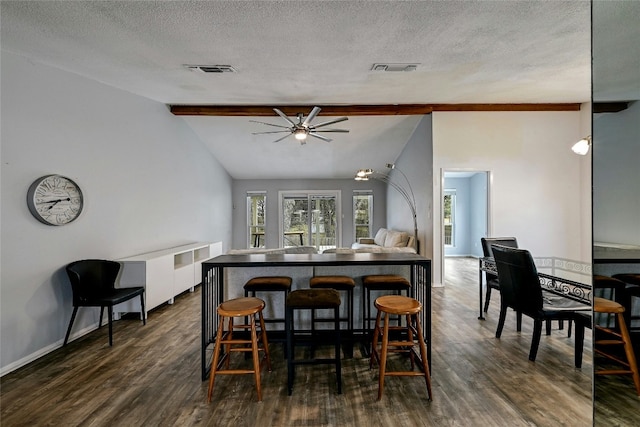 dining room with plenty of natural light, vaulted ceiling with beams, dark wood-type flooring, and a textured ceiling