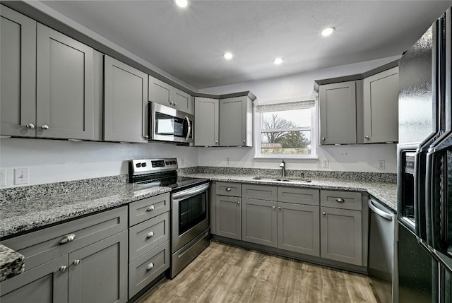 kitchen featuring sink, hardwood / wood-style flooring, gray cabinetry, stainless steel appliances, and light stone countertops