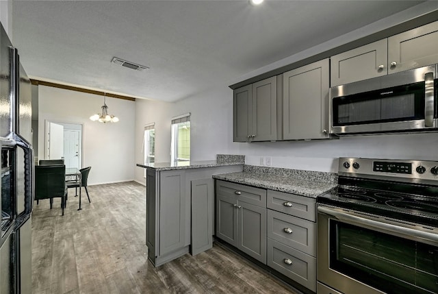 kitchen with gray cabinetry, light stone counters, kitchen peninsula, and appliances with stainless steel finishes