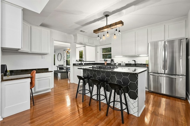 kitchen featuring appliances with stainless steel finishes, a breakfast bar area, white cabinets, hanging light fixtures, and a center island