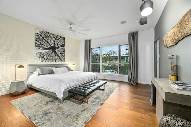 bedroom featuring hardwood / wood-style flooring, brick wall, and ceiling fan