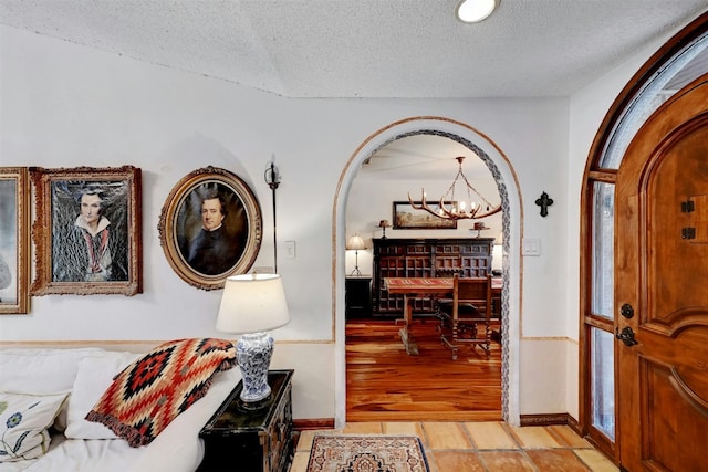 hall with a chandelier, arched walkways, light wood-style flooring, and a textured ceiling