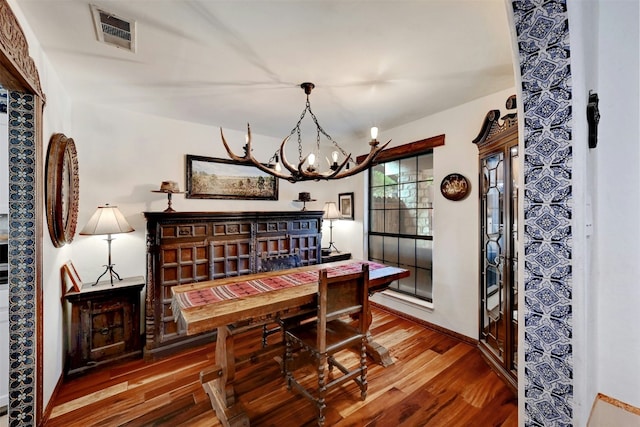 dining space with wood finished floors, visible vents, and a notable chandelier