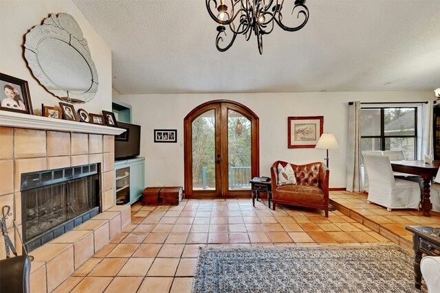 living room with light tile patterned flooring, a chandelier, a tiled fireplace, a textured ceiling, and french doors