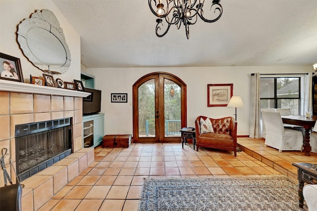 living area featuring light tile patterned floors, a textured ceiling, a tile fireplace, french doors, and an inviting chandelier