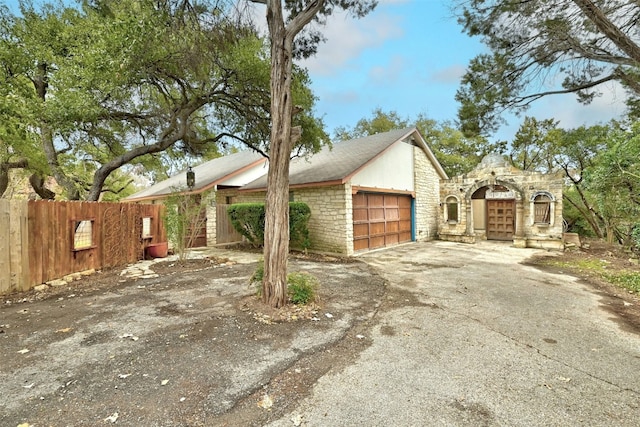 view of side of property with a garage, stone siding, fence, and driveway