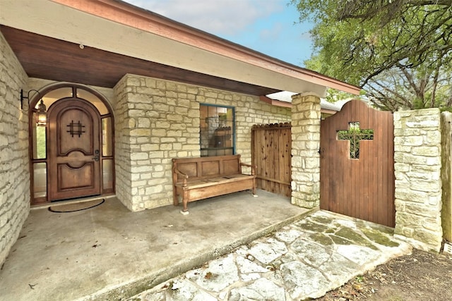 doorway to property featuring stone siding, a gate, and fence