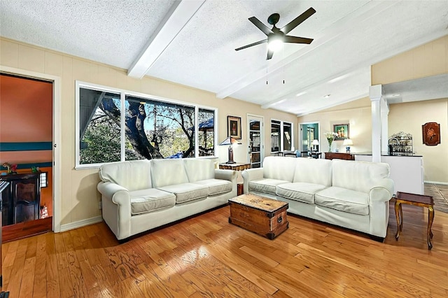 living room with ceiling fan, light hardwood / wood-style flooring, a textured ceiling, and vaulted ceiling with beams