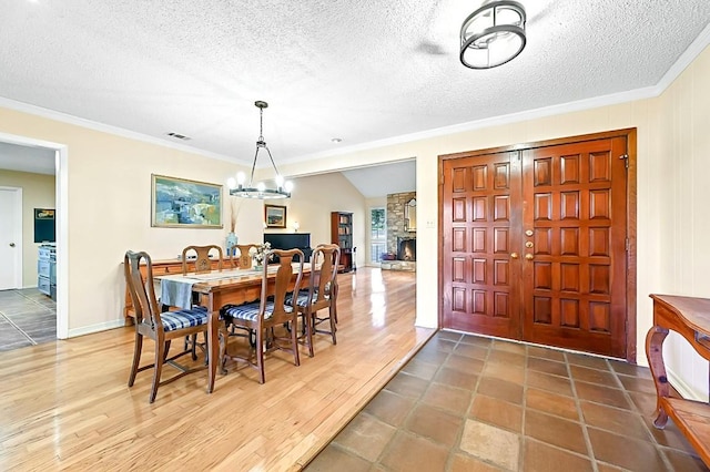 dining space featuring a textured ceiling, ornamental molding, a notable chandelier, a fireplace, and hardwood / wood-style floors