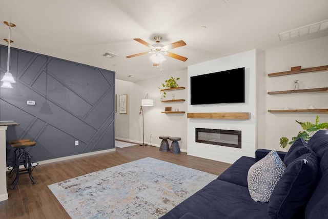 living room featuring dark wood-style floors, visible vents, a ceiling fan, and a glass covered fireplace