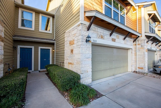 view of exterior entry with a garage, stone siding, and concrete driveway