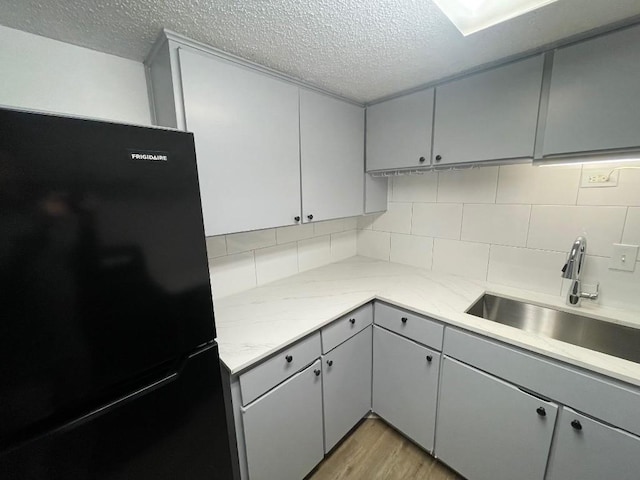 kitchen featuring black refrigerator, backsplash, gray cabinetry, and sink