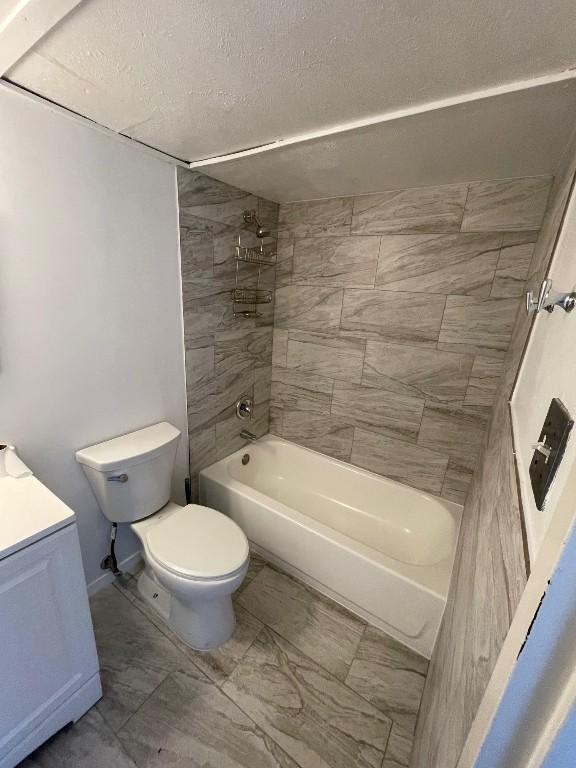 full bathroom featuring tiled shower / bath, vanity, toilet, and a textured ceiling