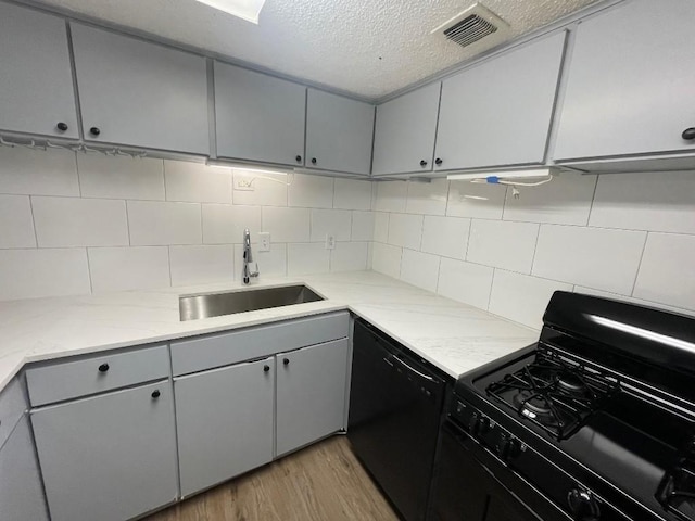 kitchen with gray cabinets, tasteful backsplash, sink, black appliances, and light wood-type flooring