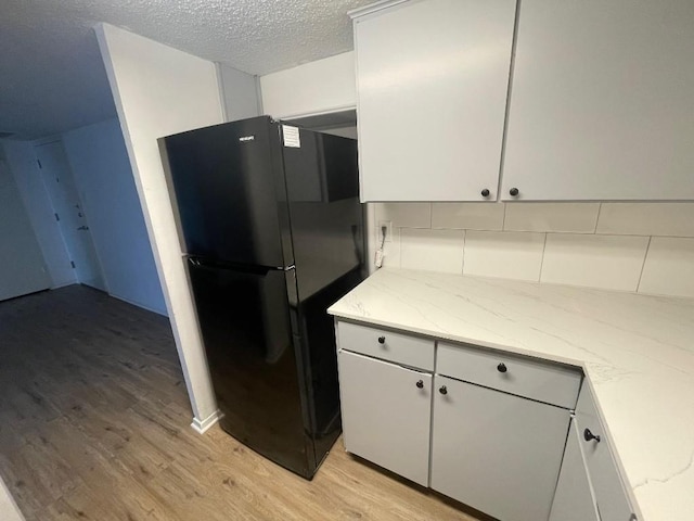 kitchen with white cabinetry, tasteful backsplash, light stone countertops, light hardwood / wood-style floors, and black fridge