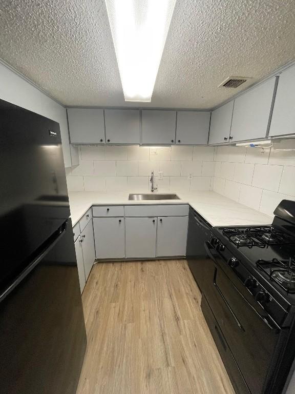 kitchen featuring gray cabinets, sink, black range with gas stovetop, decorative backsplash, and light hardwood / wood-style floors