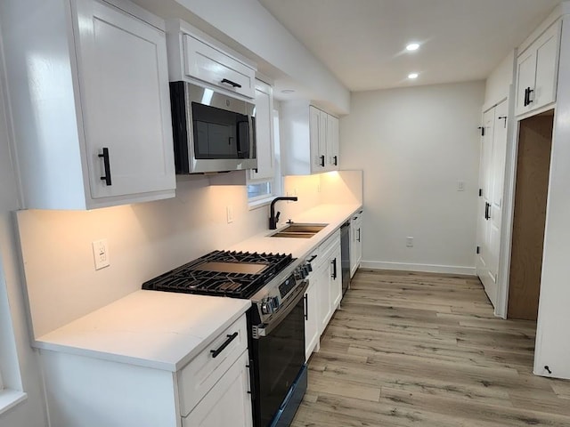 kitchen featuring stainless steel appliances, white cabinetry, sink, and light hardwood / wood-style flooring