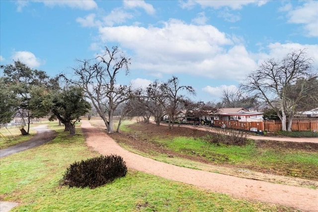 view of property's community with dirt driveway, a lawn, and fence