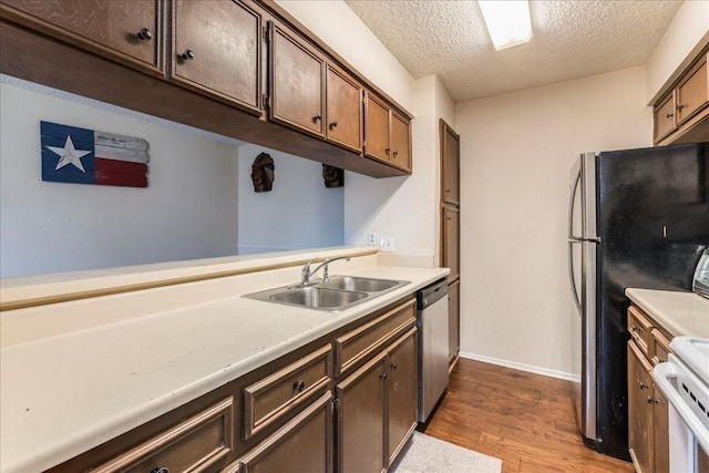 kitchen with sink, stove, a textured ceiling, stainless steel dishwasher, and light wood-type flooring