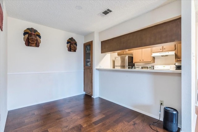 kitchen with visible vents, dark wood finished floors, freestanding refrigerator, light countertops, and under cabinet range hood