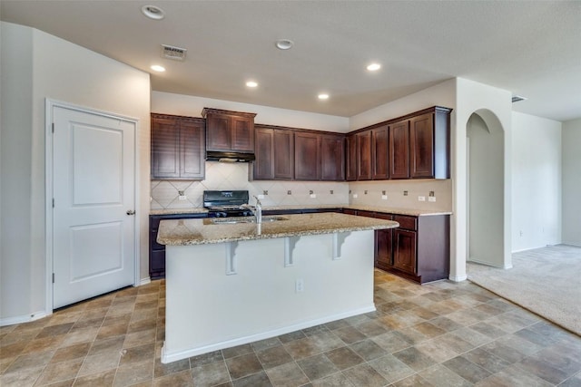 kitchen featuring black stove, sink, a breakfast bar area, a kitchen island with sink, and light stone countertops