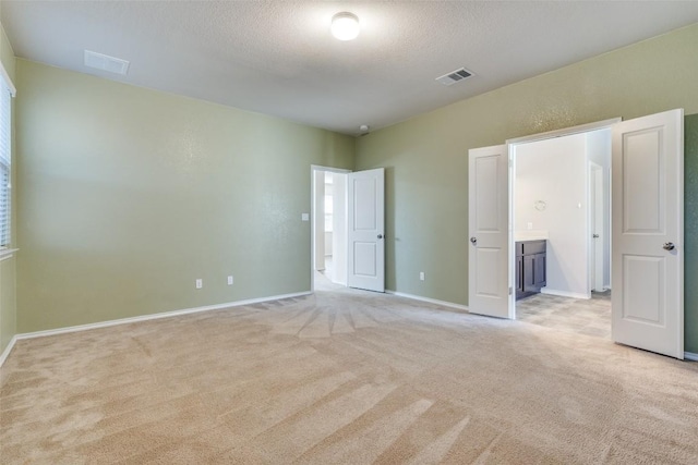 unfurnished bedroom featuring connected bathroom, light colored carpet, and a textured ceiling