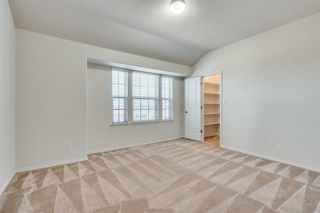 unfurnished bedroom with light colored carpet, a spacious closet, vaulted ceiling, and a closet