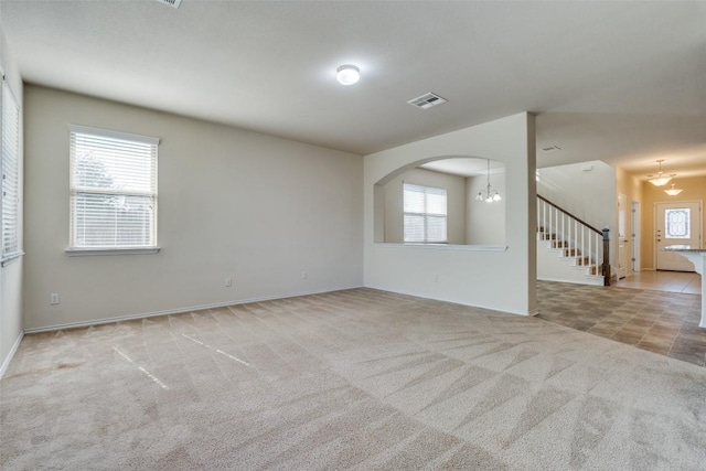 empty room featuring a notable chandelier, a wealth of natural light, and light colored carpet