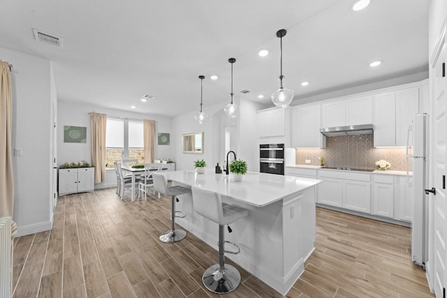 125 Jasmine Ln, Marble Falls, TX 78654 - kitchen with under cabinet range hood, black appliances, recessed lighting, tasteful backsplash, and light wood-type flooring