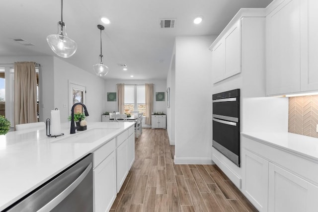 kitchen featuring double oven, decorative light fixtures, dishwasher, and white cabinets