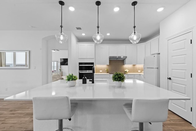 125 Jasmine Ln, Marble Falls, TX 78654 - kitchen with freestanding refrigerator, multiple ovens, under cabinet range hood, wood finish floors, and white cabinets