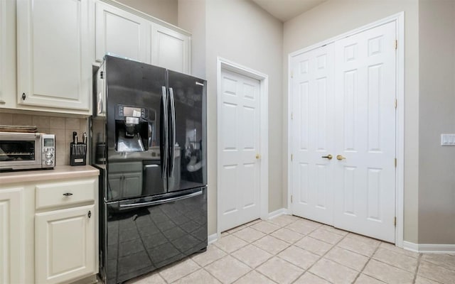 kitchen with tasteful backsplash, light tile patterned floors, white cabinets, and black refrigerator with ice dispenser