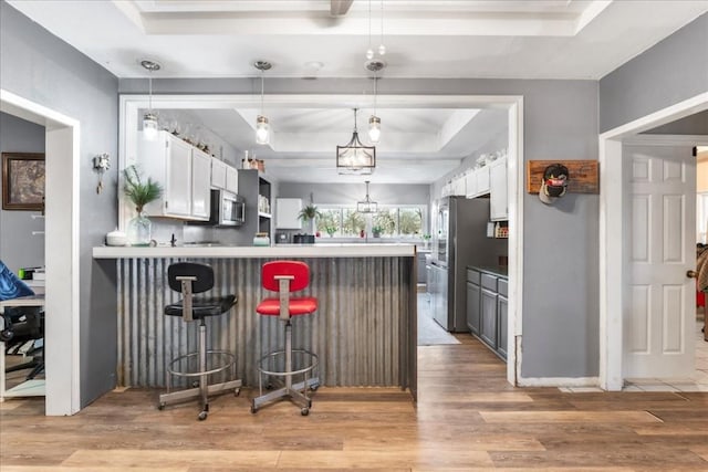 kitchen with white cabinetry, stainless steel appliances, a tray ceiling, a kitchen bar, and kitchen peninsula