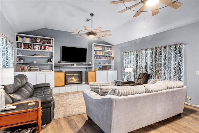 living room featuring built in shelves, vaulted ceiling, light hardwood / wood-style flooring, a tile fireplace, and ceiling fan