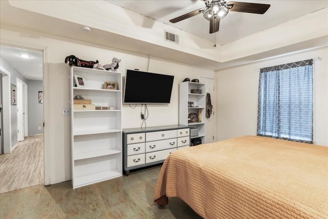 bedroom with a tray ceiling, wood-type flooring, and ceiling fan