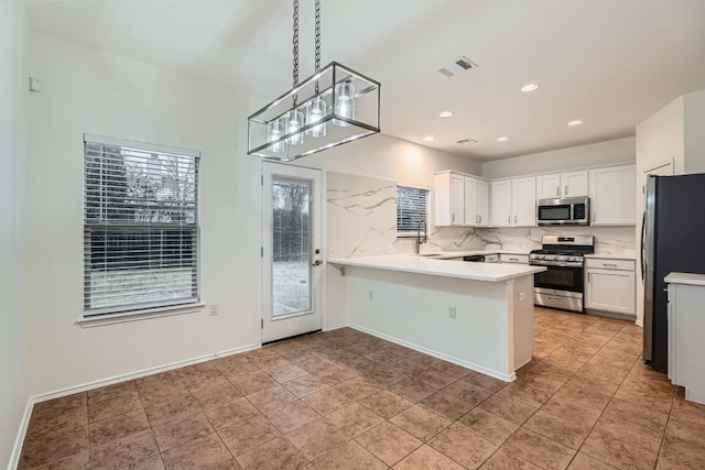 kitchen with kitchen peninsula, pendant lighting, stainless steel appliances, decorative backsplash, and white cabinets