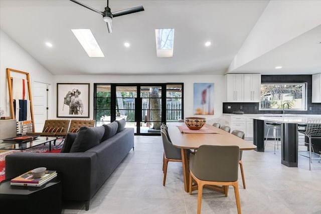 living room with ceiling fan, vaulted ceiling with skylight, and sink