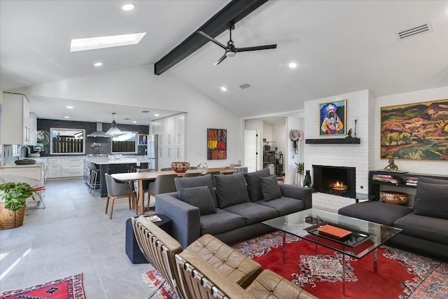 tiled living room featuring ceiling fan, a skylight, high vaulted ceiling, a brick fireplace, and beamed ceiling