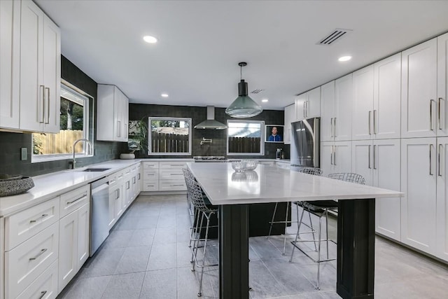 kitchen with white cabinetry, a kitchen island, wall chimney exhaust hood, and appliances with stainless steel finishes