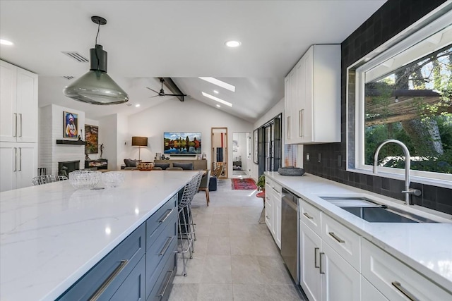 kitchen with sink, dishwasher, lofted ceiling with skylight, tasteful backsplash, and white cabinets