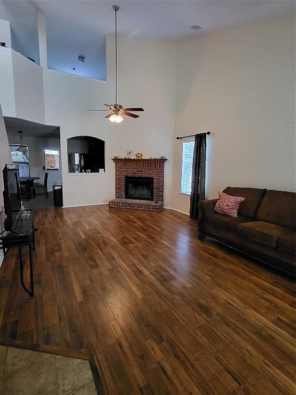 living room featuring a high ceiling, dark wood-type flooring, a fireplace, and ceiling fan