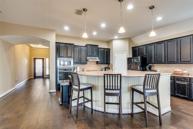 kitchen featuring decorative backsplash, stainless steel appliances, decorative light fixtures, and a center island with sink