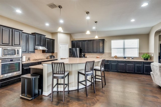 kitchen with a breakfast bar area, tasteful backsplash, appliances with stainless steel finishes, an island with sink, and pendant lighting