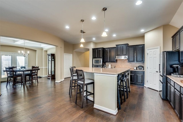 kitchen with stainless steel appliances, a center island with sink, backsplash, and decorative light fixtures