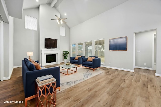 living room with ceiling fan, beam ceiling, light hardwood / wood-style flooring, and a high ceiling