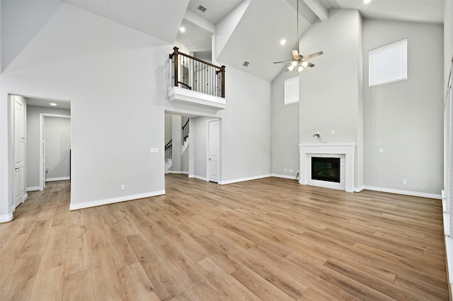 unfurnished living room featuring beamed ceiling, ceiling fan, light hardwood / wood-style floors, and high vaulted ceiling