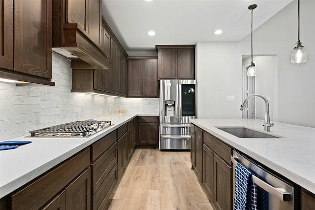 kitchen with sink, tasteful backsplash, decorative light fixtures, appliances with stainless steel finishes, and light hardwood / wood-style floors