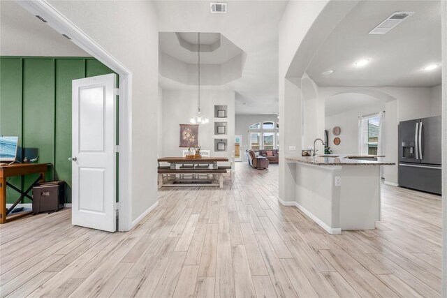 kitchen featuring stainless steel fridge with ice dispenser, decorative light fixtures, light stone counters, kitchen peninsula, and light wood-type flooring