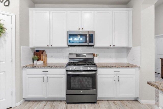 kitchen with stainless steel appliances, white cabinetry, tasteful backsplash, and light stone counters